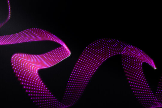 Pink and purple neon flowing wave of light as trail with dotted stripes on black background, pattern. Abstract background with motion light effect, light painting in disco style.