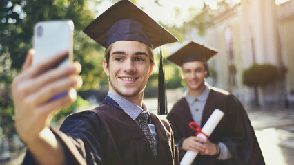 Two happy graduates taking selfie with mobile phone in the university campus.