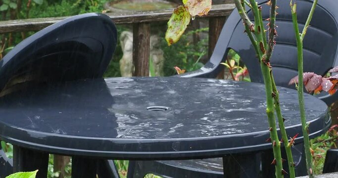 Short full HD 4K video clip of heavy rain falling on a black plastic table in a garden