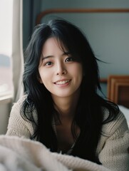 A woman with long black hair is smiling and wearing a white sweater