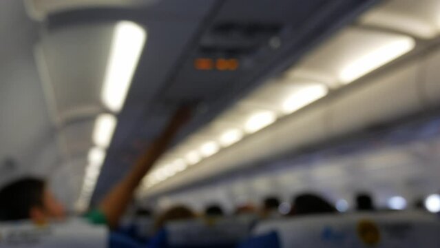 out of focusing inside plane cabin from the back with passengers sitting on seats, Blurry defocused interior of modern airplane while people taking their seats