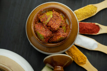 Homemade Mango Pickle or aam ka achar Kairi Loncha stored or preserved in China clay pot with Ingredients.