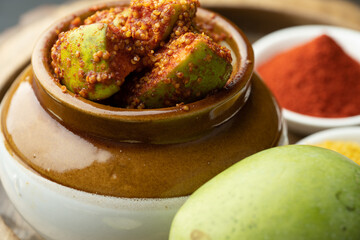 Homemade Mango Pickle or aam ka achar Kairi Loncha stored or preserved in China clay pot with Ingredients.