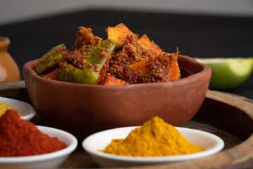 Homemade Mango Pickle or aam ka achar Kairi Loncha stored or preserved in China clay pot with Ingredients.