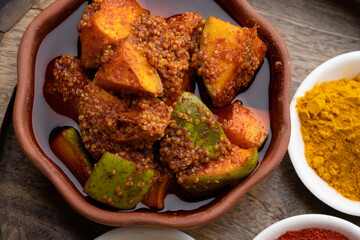 Homemade Mango Pickle or aam ka achar Kairi Loncha stored or preserved in China clay pot with Ingredients.