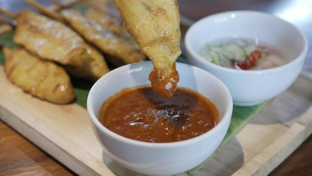 hand grabing satay skewer bbq chicken on a plate in traditional singaporean or malaysian style in traditional cruisine dipping into the sauce