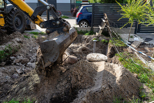 Using an excavator to bury a 10 m3 concrete septic tank located in the garden next to the house.