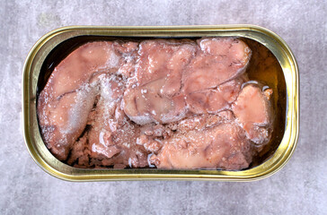 Canned cod liver in open metal tin with oil on the gray table