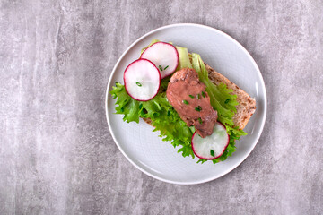 Cod liver served on bread slice with lettuce leaf and radish on the white plate on gray. Exquisite appetizer. Top view - 765747455