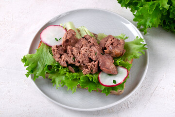 Cod liver served on bread slice with lettuce leaf and radish on the white plate. Exquisite appetizer - 765747492