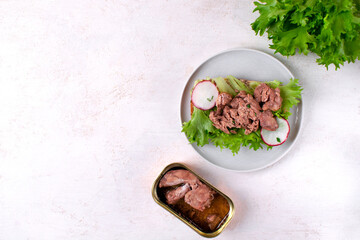 Cod liver served on bread slice with lettuce leaf and radish on the white plate and a tin of the product. Exquisite appetizer. Mockup with copy space