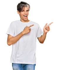 Young hispanic man wearing casual white tshirt smiling and looking at the camera pointing with two hands and fingers to the side.