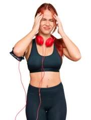 Poster Young redhead woman wearing gym clothes and using headphones suffering from headache desperate and stressed because pain and migraine. hands on head. © Krakenimages.com