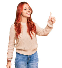 Young redhead woman wearing casual winter sweater looking proud, smiling doing thumbs up gesture to...