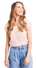 Young beautiful caucasian woman with blond hair wearing casual clothes looking away to side with smile on face, natural expression. laughing confident.