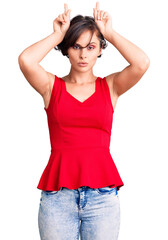 Beautiful young woman with short hair wearing casual style with sleeveless shirt doing funny gesture with finger over head as bull horns