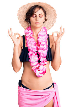 Beautiful young woman with short hair wearing bikini and hawaiian lei relax and smiling with eyes closed doing meditation gesture with fingers. yoga concept.