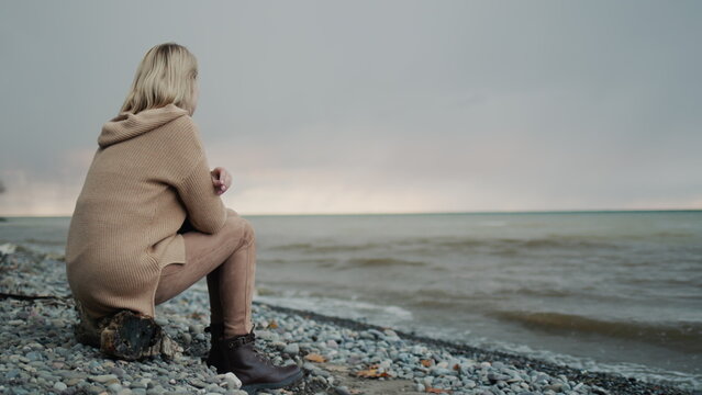 The view from the back of a woman, admiring the stormy sky above the sea. Sits on the shore