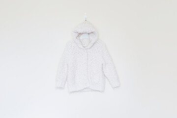 Babies hooded snuggly cardigan in cream white, hung against a cream background 