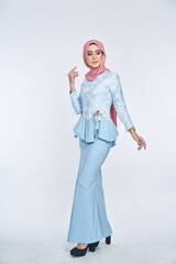 Beautiful female model wearing blue peplum dress with hijab, a modern lifestyle outfit for Muslim woman, sitting on a chair isolated over white background. Eidul fitri fashion and beauty concept.