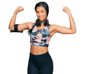 Beautiful hispanic woman wearing sportswear and headphones showing arms muscles smiling proud. fitness concept.
