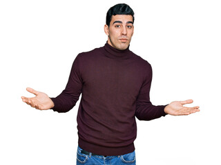 Handsome hispanic man wearing casual turtleneck sweater clueless and confused expression with arms...