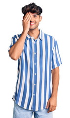 Young hispanic man wearing casual clothes covering one eye with hand, confident smile on face and surprise emotion.