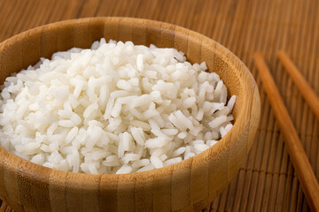 Detail of cooked white rice in a dark wood bowl next to chopsticks on bamboo matt. - 765783273