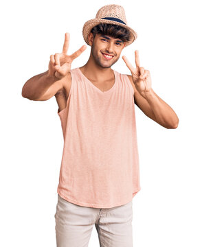 Young hispanic man wearing summer hat smiling looking to the camera showing fingers doing victory sign. number two.