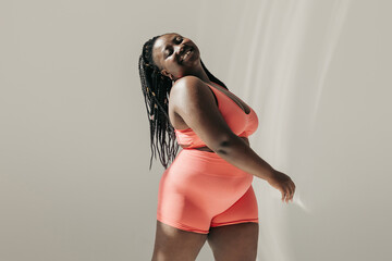Full length of happy African plus size woman in sportswear radiating self love while standing in fitness studio - 765783666