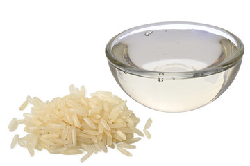 Rice syrup in a glass bowl next to a pile of uncooked white rice isolated on white.