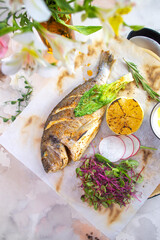 Grilled fish Dorado with lemon and herbs on a white background top view.
