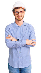 Handsome young man with bear wearing architect hardhat happy face smiling with crossed arms looking...