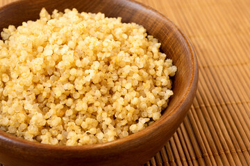 Detail of cooked white quinoa in a dark wood bowl on bamboo matt. - 765784603