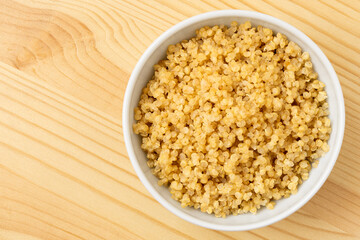 Cooked white quinoa in a white ceramic bowl isolated on light wood from above. - 765785213