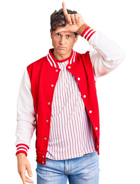 Young handsome man wearing baseball uniform making fun of people with fingers on forehead doing loser gesture mocking and insulting.