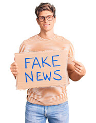 Young handsome man holding fake news banner smiling happy pointing with hand and finger