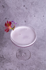 Elegant pink cocktail in a glass with a floral side dish on a gray background top view