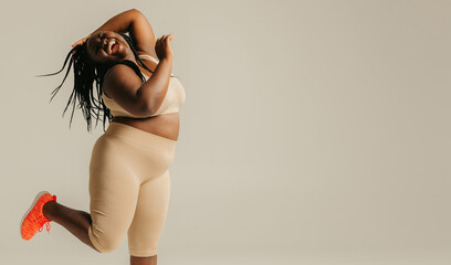 Full length happy plus size African woman in sportswear dancing on studio background - 765787632