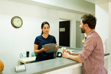 Male patient at the reception desk of the clinic talking to the nurse
