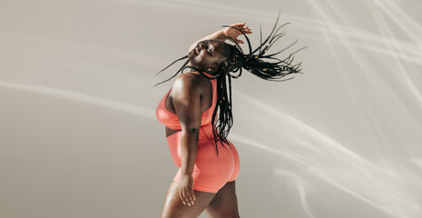 Joyful African plus size woman in sportswear dancing and radiating self-love in fitness studio - 765788418