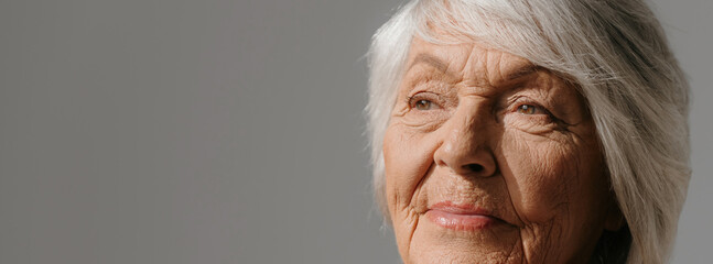Close-up of gray hair senior woman looking away against grey background