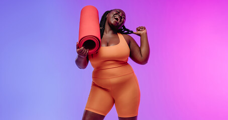 Happy African plus size woman in sportswear carrying exercise mat and smiling on vibrant background - 765791824