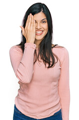 Young hispanic woman wearing casual clothes covering one eye with hand, confident smile on face and surprise emotion.