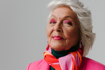 Elegant elderly woman with make-up wearing fashionable clothing and radiating self-love on grey background - 765797020