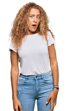Beautiful caucasian teenager girl wearing casual white tshirt in shock face, looking skeptical and sarcastic, surprised with open mouth