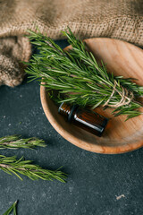 A bottle of essential oil with fresh rosemary twigs on a dark background