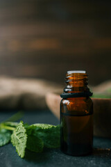 Bottle of essential oil with mint on wooden background