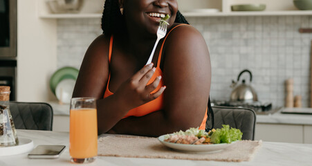 Close-up of plus size African woman enjoying healthy food for lunch at the kitchen