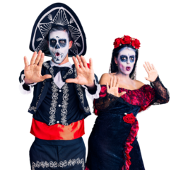 Young couple wearing mexican day of the dead costume over background doing stop gesture with hands palms, angry and frustration expression